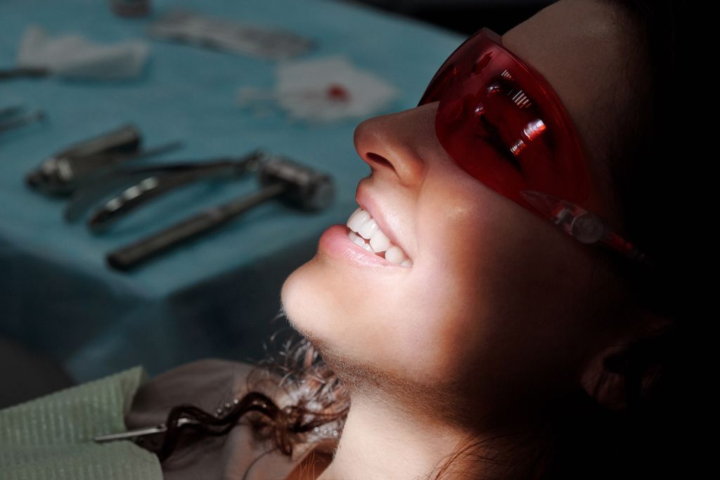 Close-up of a woman smiling with protective glasses at a dental clinic, highlighting her teeth.